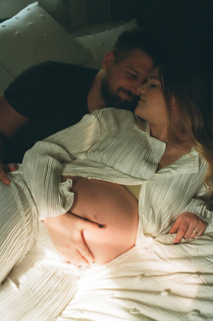 husband and pregnant wife laying in bed cuddling