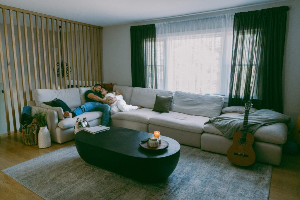 husband and wife cuddling on their couch and holding her pregnant belly