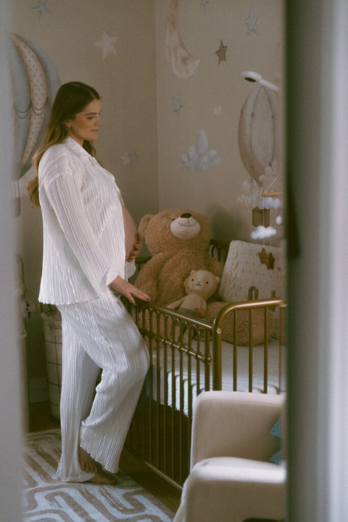 wife holding her belly in the decorated baby's nursery