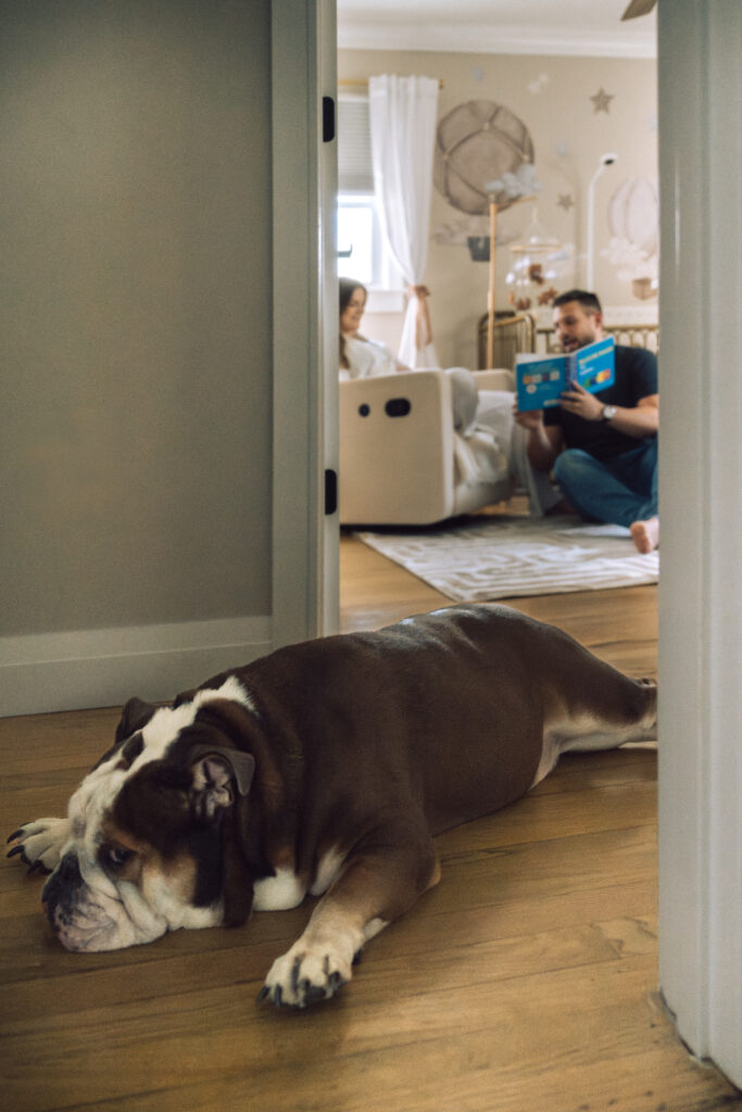 husband and wife reading a children's book in the nursery while the dog lays down in the hallway