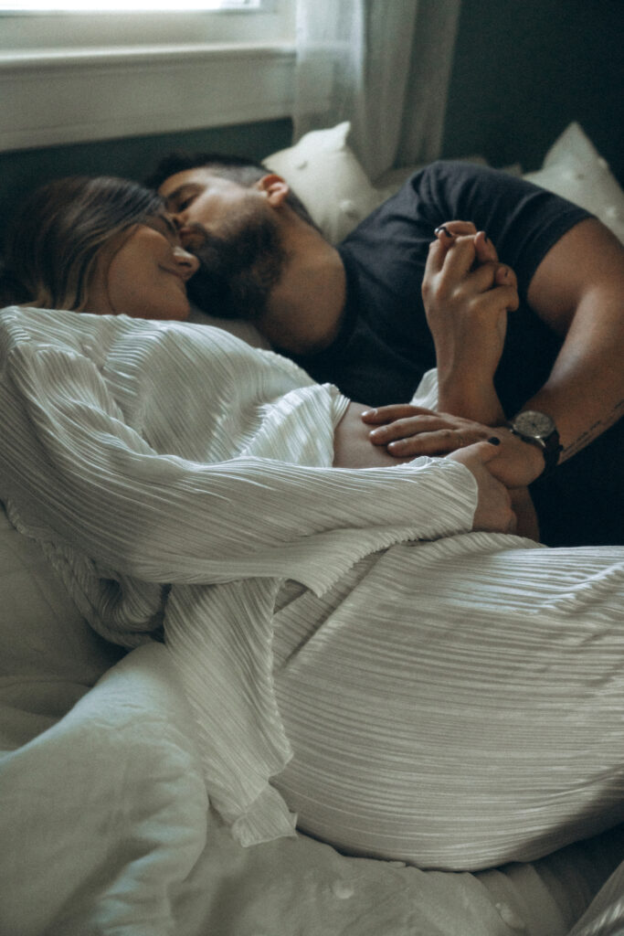 husband kissing his wife's forehead while laying in bed cuddling