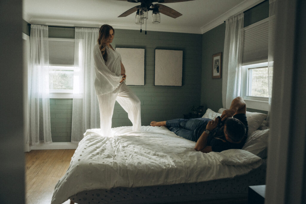 husband taking photo of pregnant wife while she stands on the bed