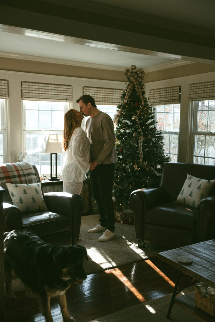 husband and wife kissing in front of their christmas tree