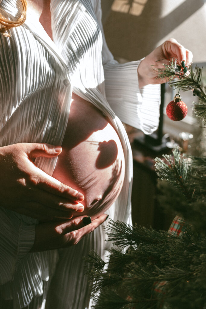 pregnant wife hanging an ornament on the tree while the shadow reflects on her belly