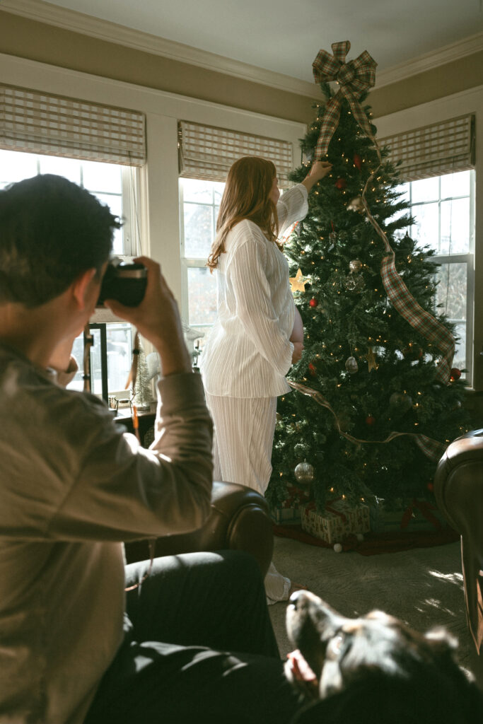 husband taking a picture of his wife decorating the christmas tree