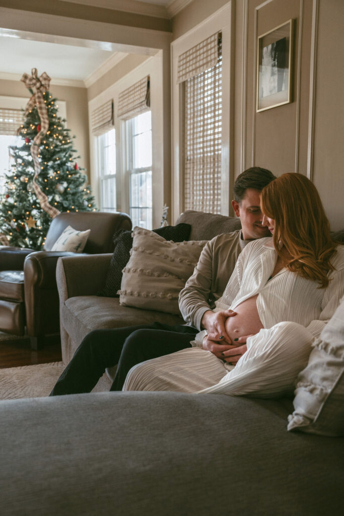 husband and wife snuggling on the couch while he holds her pregnant belly