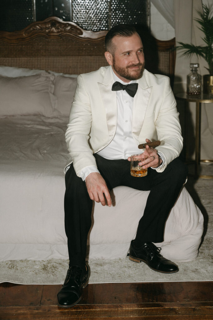 husband smiling in his suit while holding a drink and cigar