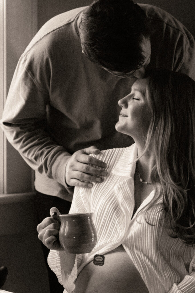 husband kissing wife on her forehead while she is enjoying a cup of tea