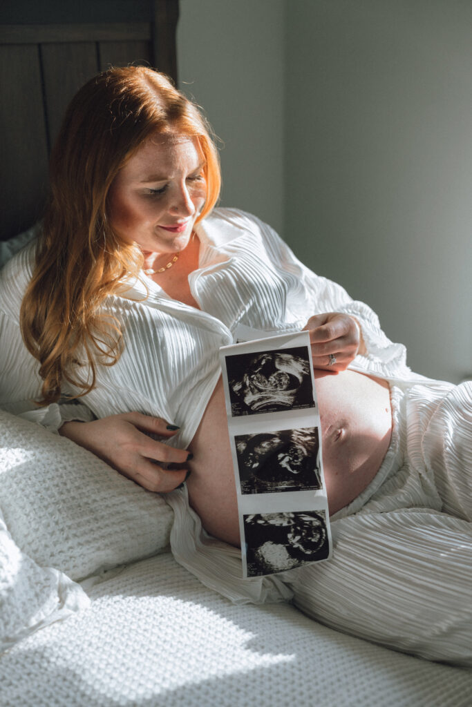 wife laying on the bed with her ultrasound photos