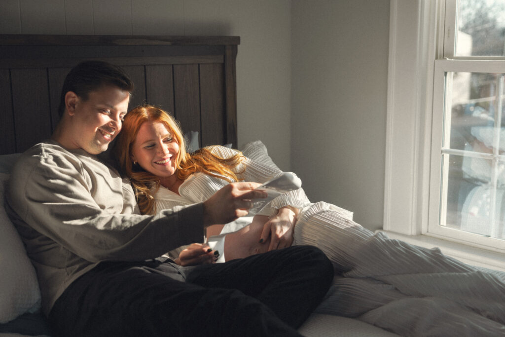 husband and wife snuggling in bed while looking at their ultrasound photos