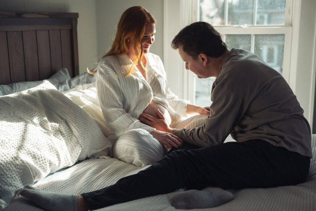 husband and wife on bed while he admires her pregnant belly