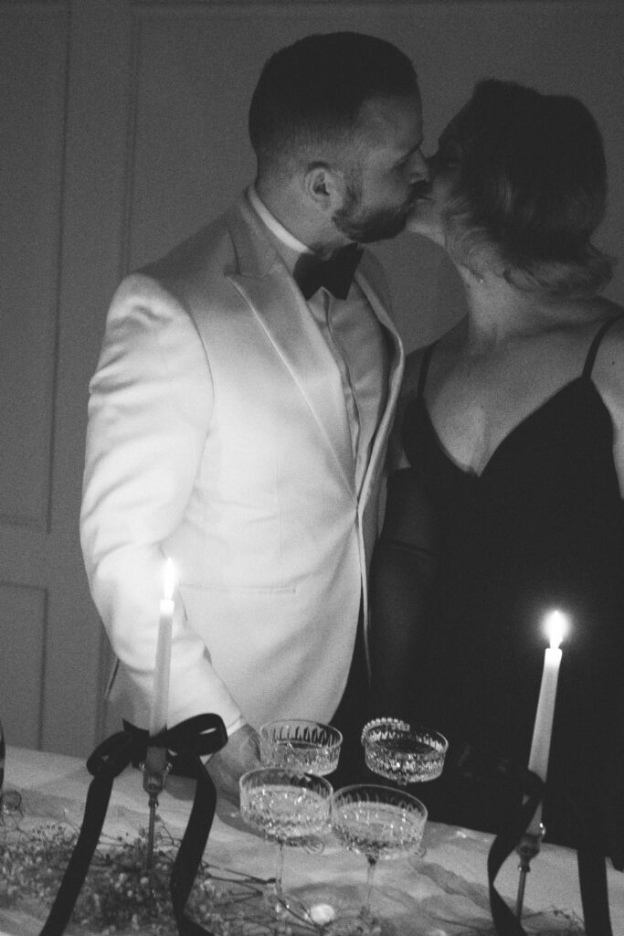 husband and wife kissing behind mini champagne tower