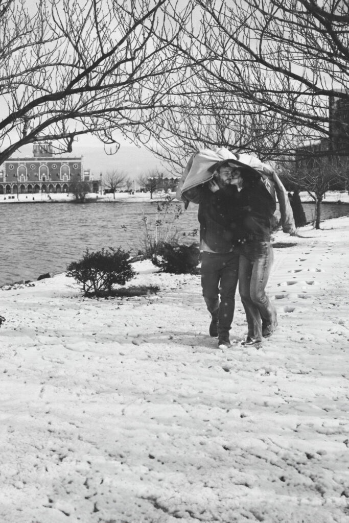 the couple outside kissing in the snow with a jacket over their heads