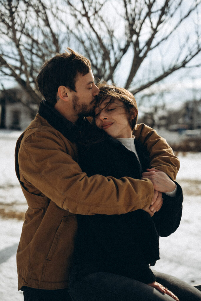 the couples posing outside while the man is kissing his fiance on the forehead