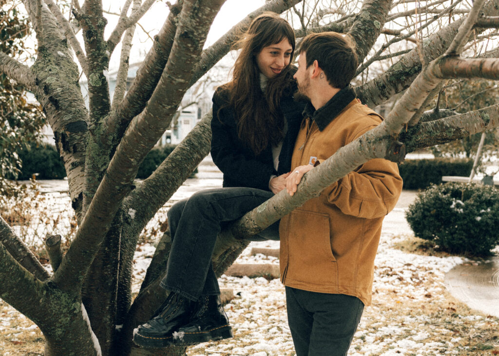 couple smiling at each other while the woman is sitting in a tree