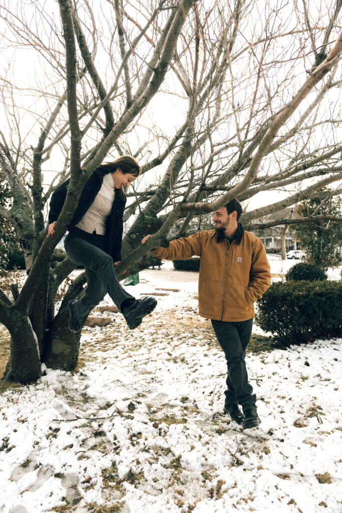 the couple smiling while the women jumps towards her fiance while getting down from the tree