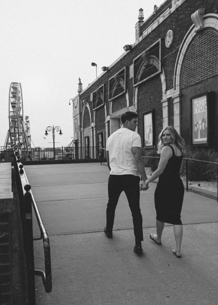 couple on boardwalk holding hands while the woman looks over her shoulder at the camera