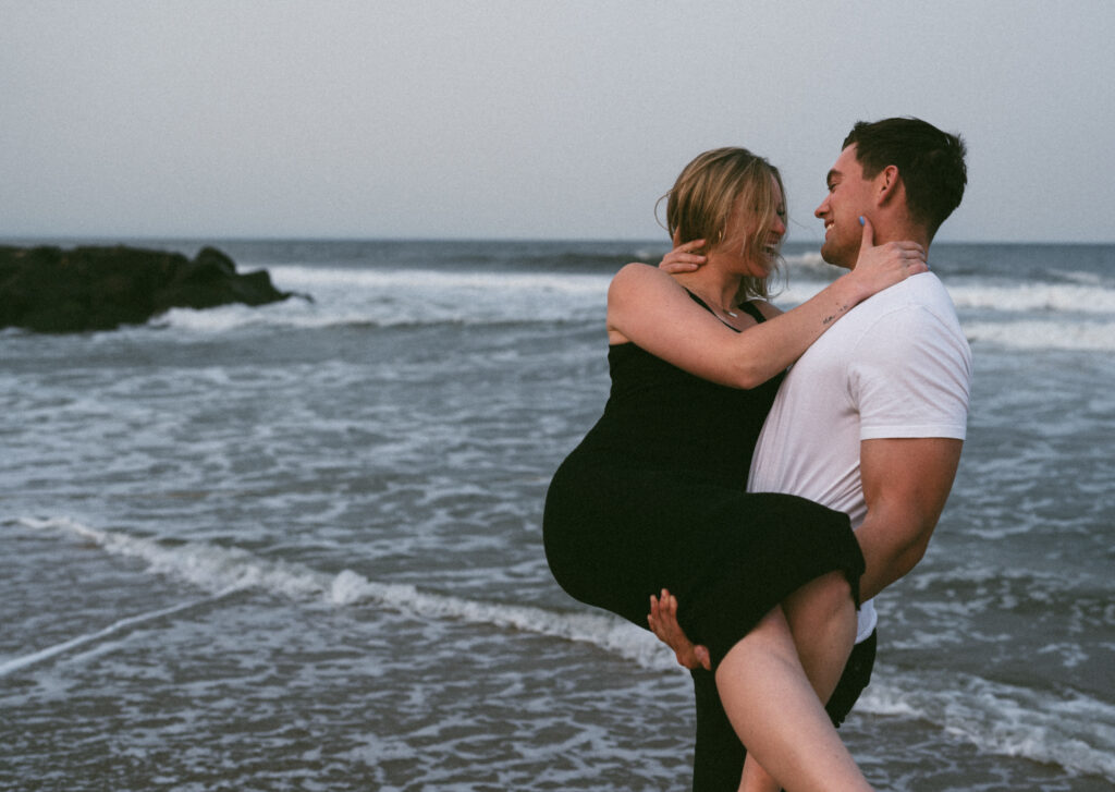 couple on beach where the man is holding his partner in his arms while they both laugh