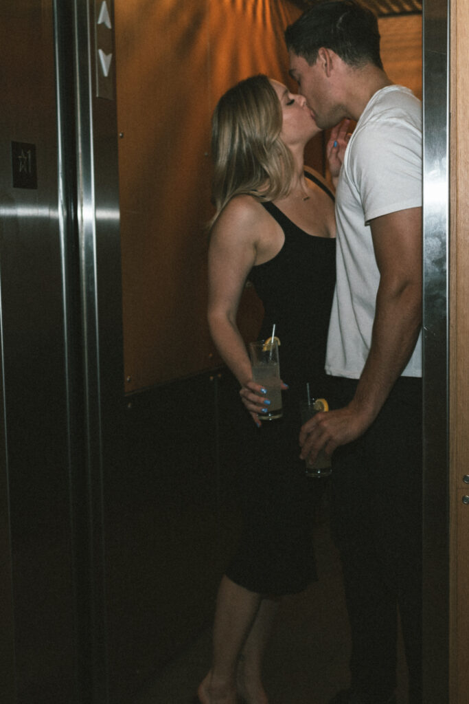 couple kissing in the elevator while holding drinks