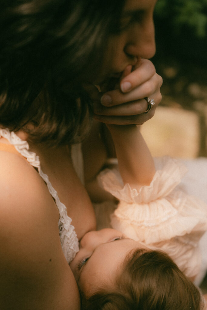 mother breastfeeding her daughter while she kisses her hand