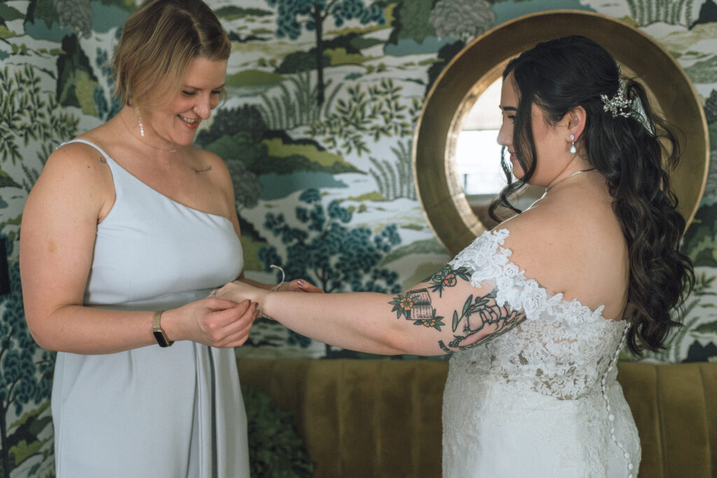 bridesmaid helping the bride put a bracelet on her wrist