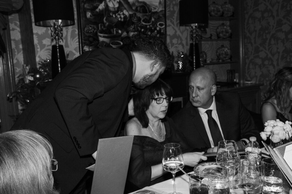 groom kissing his mom on the head while she is sitting at the dinner table